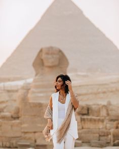 a woman is standing in front of the pyramids and talking on her cell phone