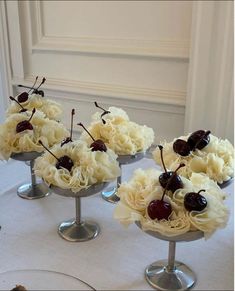 four small vases with cherries and flowers on a table