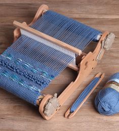 a blue weaving machine with two skeins of yarn next to it on a wooden surface