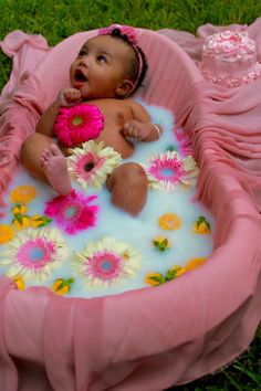 a baby in a pink bath tub with flowers on the bottom and green grass around it