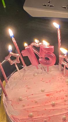 a pink birthday cake with lit candles and the number 75 on it's top