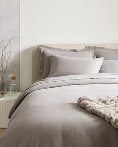 an unmade bed with grey sheets and pillows