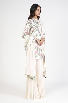 Ivory kurta with collar, placket, all over tropical trees pattern and multi color thread embroidery. Paired with sharara with intricated pleated panel and embroidered bordered dupatta.
Components: 3
Pattern: Embroidered
Type Of Work: Thread and Bead Work
Neckline: Round Neck
Sleeve Type: Full Sleeves
Fabric: Raw Silk, Georgette
Color: Ivory
Other Details: 
Cut work dupatta hem
Bead work details on collar and placket
Kurta Closure: Front concealed placket
Occasion: Wedding,Sangeet - Aza Fashions Kurta With Collar, Tropical Trees, Kurta Sharara Set, Kurta Sharara, Sharara Set, Thread Embroidery, Full Sleeves, Cut Work, Embroidered Silk