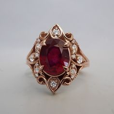 a ring with a large red stone surrounded by small white diamonds on the sides, set in gold