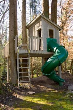 a green slide in the woods next to a tree house with a wooden deck and stairs