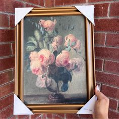 a person holding up a piece of paper to a painting on a brick wall with flowers in it