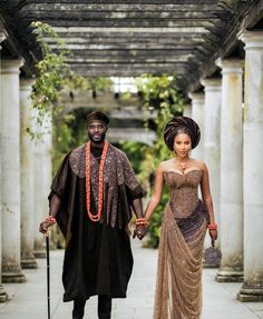 a man and woman dressed in african garb walking down a walkway holding each other's hands