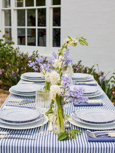 a blue and white striped table cloth with flowers in vases, plates and utensils