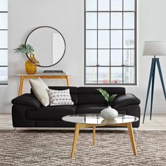 a living room with black leather couches and white pillows on top of the rug