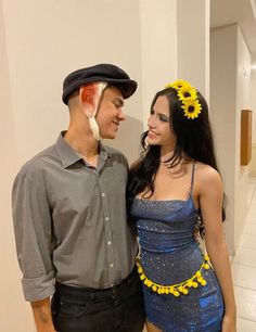 a man standing next to a woman in a blue dress and top hat with sunflowers on her head