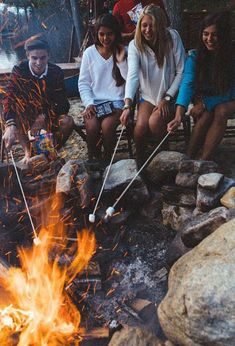 four people sitting around a campfire with marshmallows