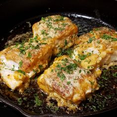 four pieces of chicken in a skillet with parmesan cheese and herbs on top