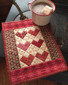 a cup of coffee sitting on top of a table next to a red and white quilt