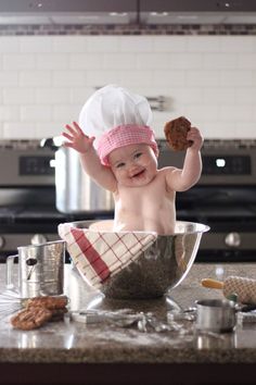 a baby wearing a chef's hat is sitting in a bowl with food on the counter