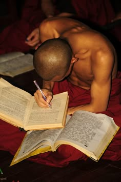 a shirtless man writing on an open book