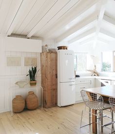 a kitchen with white walls and wooden floors has an old refrigerator in the corner, along with two stools