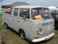 an old vw bus is parked on the grass with other cars in the background