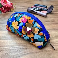 a flowered pouch sitting on top of a wooden table next to lipstick and makeup brushes