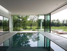 an indoor swimming pool with glass walls and doors leading to the outside area, surrounded by trees