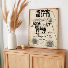 a wooden cabinet sitting next to a white vase filled with dry grass and an old poster