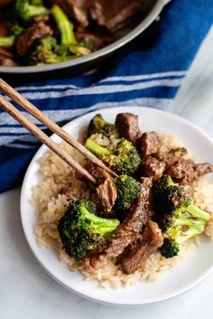 beef and broccoli stir fry on rice with chopsticks in the foreground