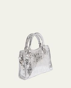 Balenciaga "Le City" top handle bag in metallic lamb leather     Rolled top handles     Detachable, adjustable shoulder/crossbody strap    Can be worn as a top handle or shoulder/crossbody bag     Zip top closure     Exterior, front zip pocket     Interior, one zip pocket     Approx. 6.3"H x 9.4"W x 2.5"D    Wipe clean    Made in Italy Silver Shoulder Bag With Top Handle And Detachable Handle, Luxury Metallic Bag With Adjustable Strap, Luxury Metallic Shoulder Bag With Adjustable Strap, Silver Satchel With Adjustable Strap And Top Handle, Silver Top Handle Shoulder Bag With Detachable Strap, Silver Top Handle Shoulder Bag, Silver Shoulder Bag With Top Carry Handle, Designer Metallic Crossbody Bag, Luxury Metallic Top Handle Bag