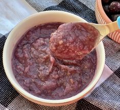 a bowl filled with meatballs on top of a checkered table cloth next to a wooden spoon