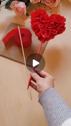 someone is making a heart out of red yarn and flowers on a table with pink roses