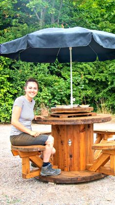 a woman sitting under an umbrella on top of a wooden table with benches underneath it