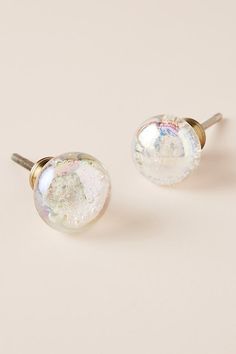 two pairs of earrings with white and iridescent designs on the front, one in gold plated setting