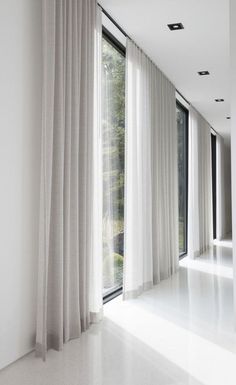 an empty room with large windows and white curtains on the outside, along with floor to ceiling windows