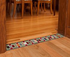 a wooden floor with a colorful tile border on the bottom and side of it in front of a dining room table