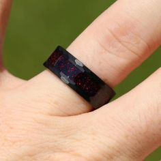 a person's hand with a ring that has red and black glitter on it