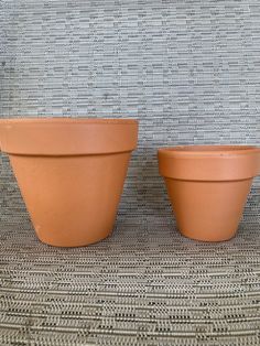 two clay pots sitting next to each other on top of a woven cloth covered surface