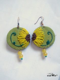 a pair of yellow and green earrings with flowers on the front, hanging from hooks