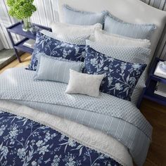 a bed with blue and white comforters in a room next to a vase filled with flowers