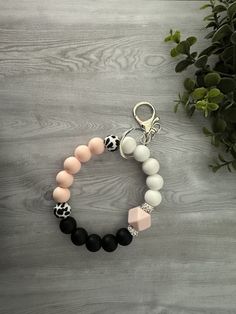 a black, white and pink beaded bracelet on a wooden table next to a potted plant