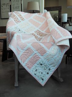 a pink and white quilt sitting on top of a wooden chair next to a lamp