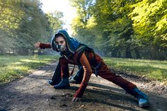 a man with a hoodie and goggles on his head is crawling down a dirt road in the woods