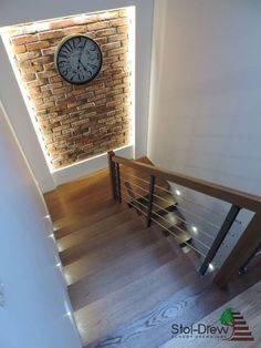 a clock mounted to the side of a brick wall next to a wooden stair case