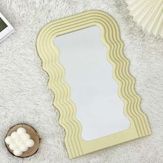 a mirror sitting on top of a white rug next to a small wooden bowl and fan