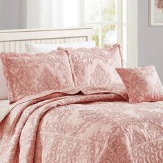 a bed with pink comforters and pillows in a room next to a white headboard