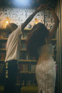 a man and woman dancing in front of a bookshelf with lights on it