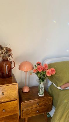 a bed with two nightstands and flowers on it next to a lamp in the corner