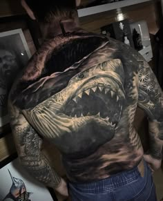 the back of a man's body covered in tattoos with a shark on it