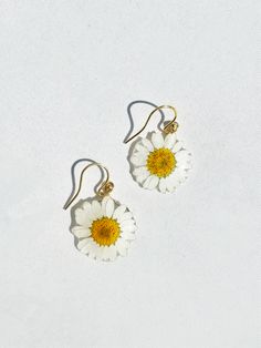 two white and yellow flowers are hanging from gold earwires on a white surface