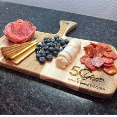 a wooden cutting board topped with meat, cheese and blueberries next to a knife