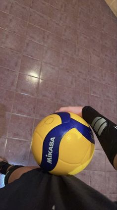 a yellow and blue soccer ball sitting on top of a person's leg in front of a tiled floor