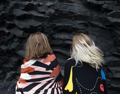 two women standing next to each other in front of black rock formations with colorful designs on them