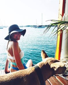 a woman in a hat sitting next to a brown dog on a wooden deck near the water